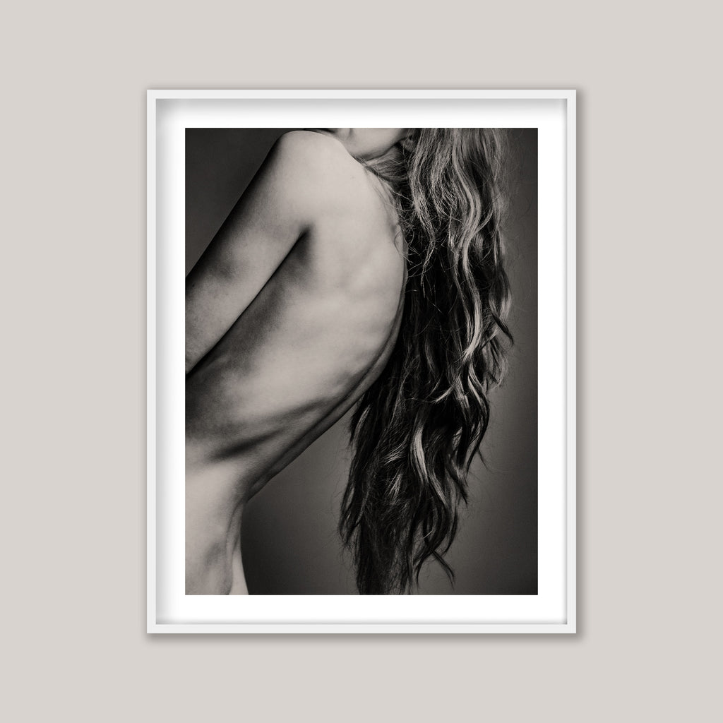 Framed black and white art print of a woman's back and hair on a plain wall.